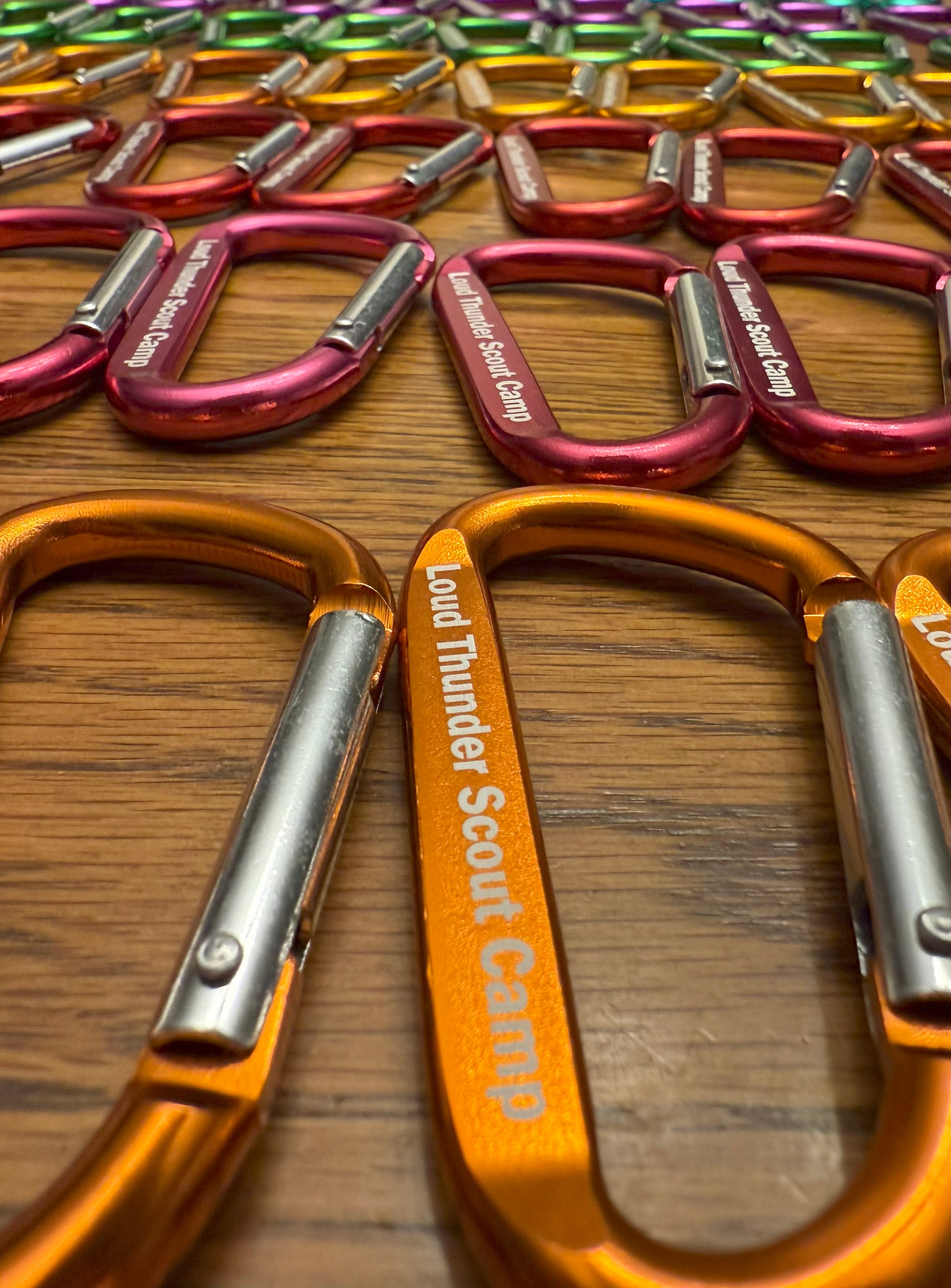 Colorful carabiners with 'Loud Thunder Scout Camp' branding on a wooden surface